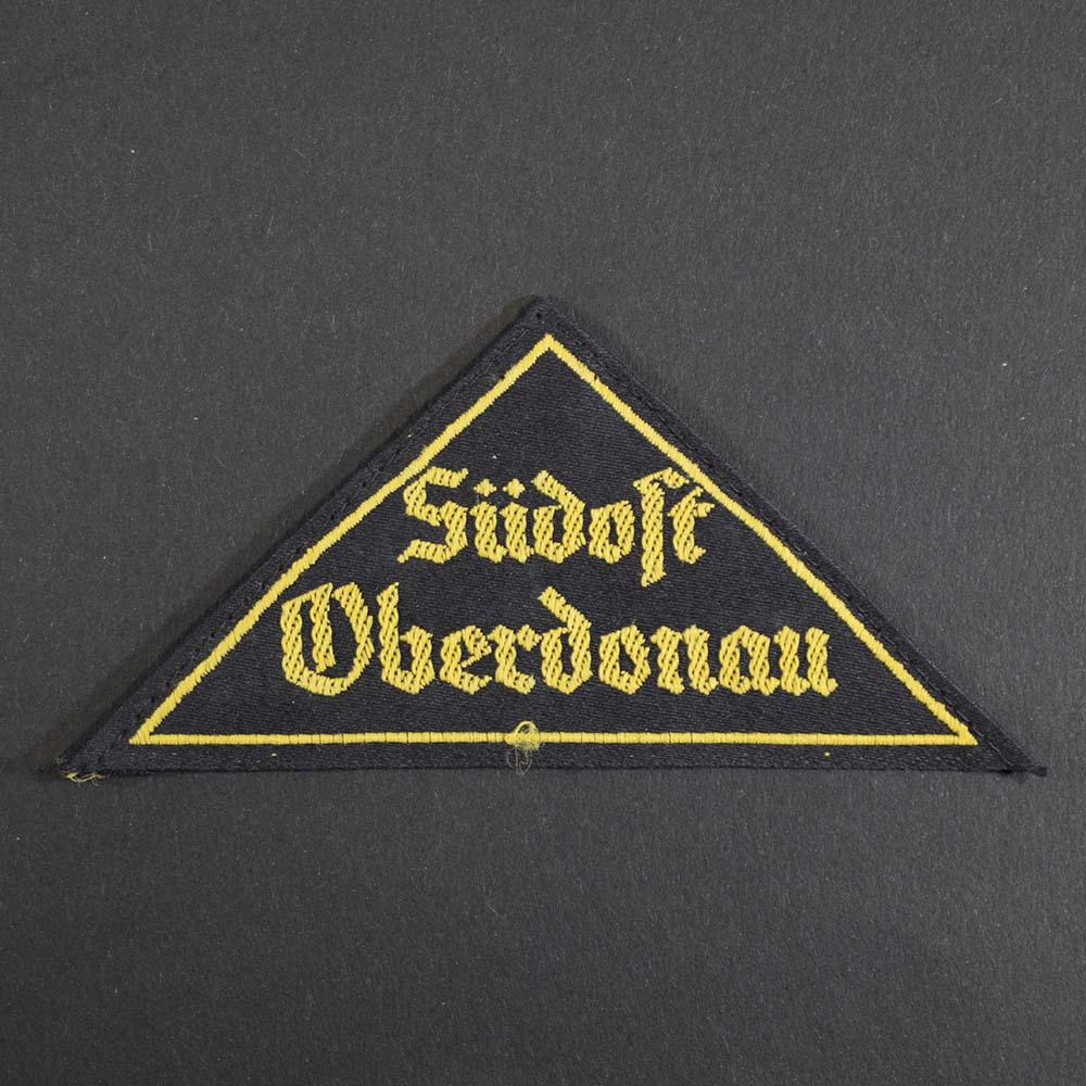Front view of the Hitler Youth District Triangle 'Südost Oberdonau', showing the black cloth triangle with yellow embroidered text, representing the regional designation worn on uniforms.