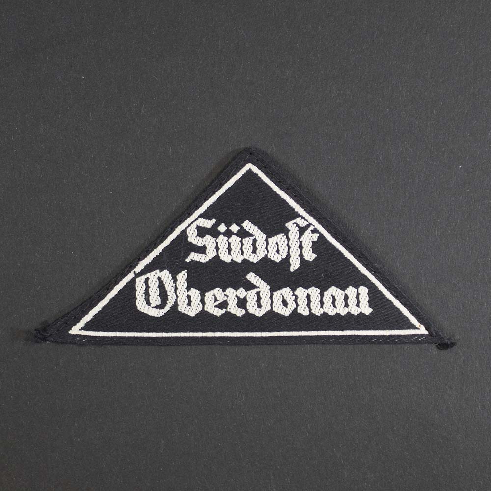 Front view of the League of German Girls District Triangle 'Südost Oberdonau', showing the black cloth triangle with white embroidered text, representing the regional designation worn on uniforms.