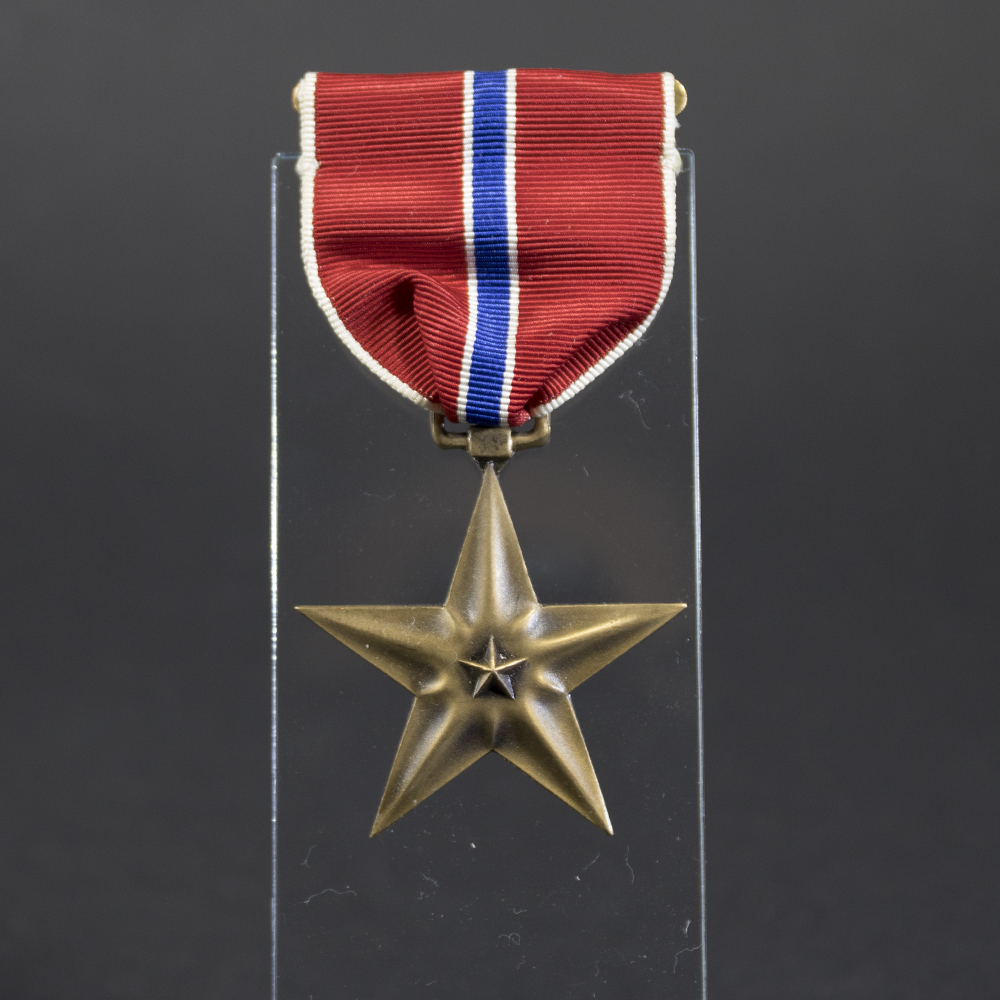 Full front view of the Bronze Star Medal, showing the five-pointed bronze star with central relief and attached ribbon in red, white, and blue.