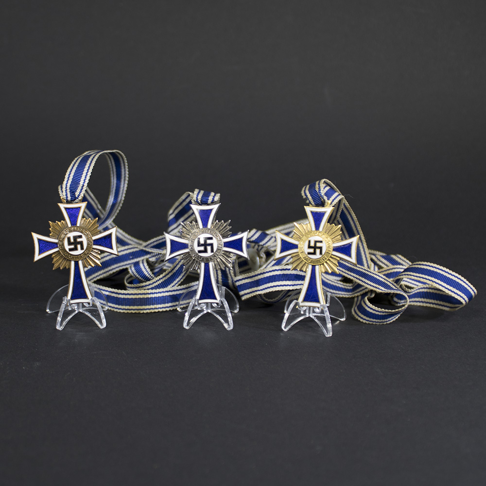 German Mother’s Cross set, featuring a white enamel cross with blue borders, a central swastika emblem, and the inscription ‘Der Deutschen Mutter’