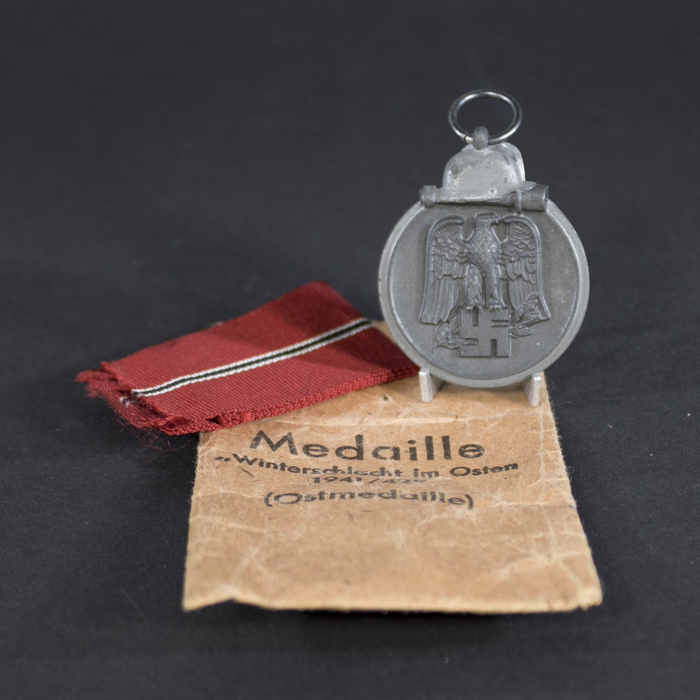 Front of a German Eastern Front Medal showing a raised design with a German eagle clutching a swastika above a crossed sword and laurel wreath, with a helmet and grenade motif at the bottom.