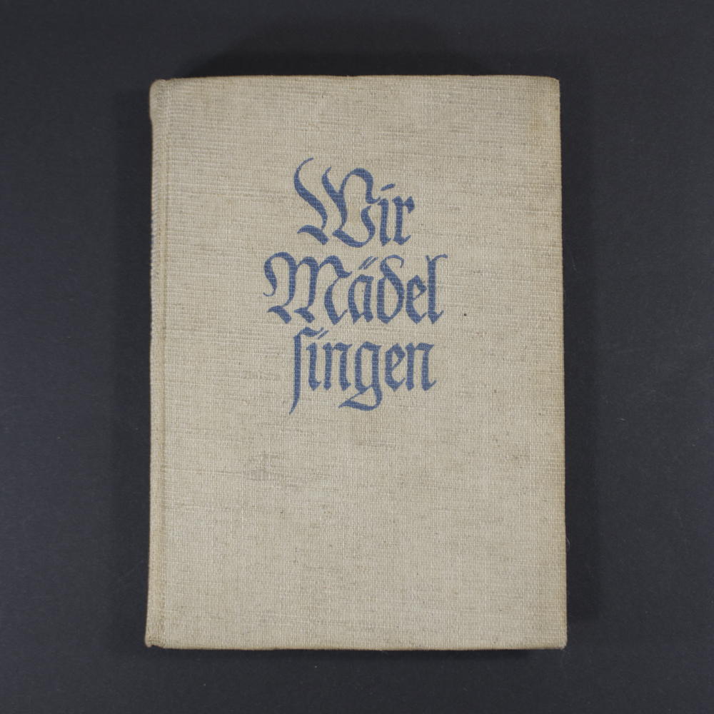 Front cover of the BDM songbook ‘Wir Mädel singen’ featuring the title in decorative Gothic script, an illustration of girls singing, and a simple border.