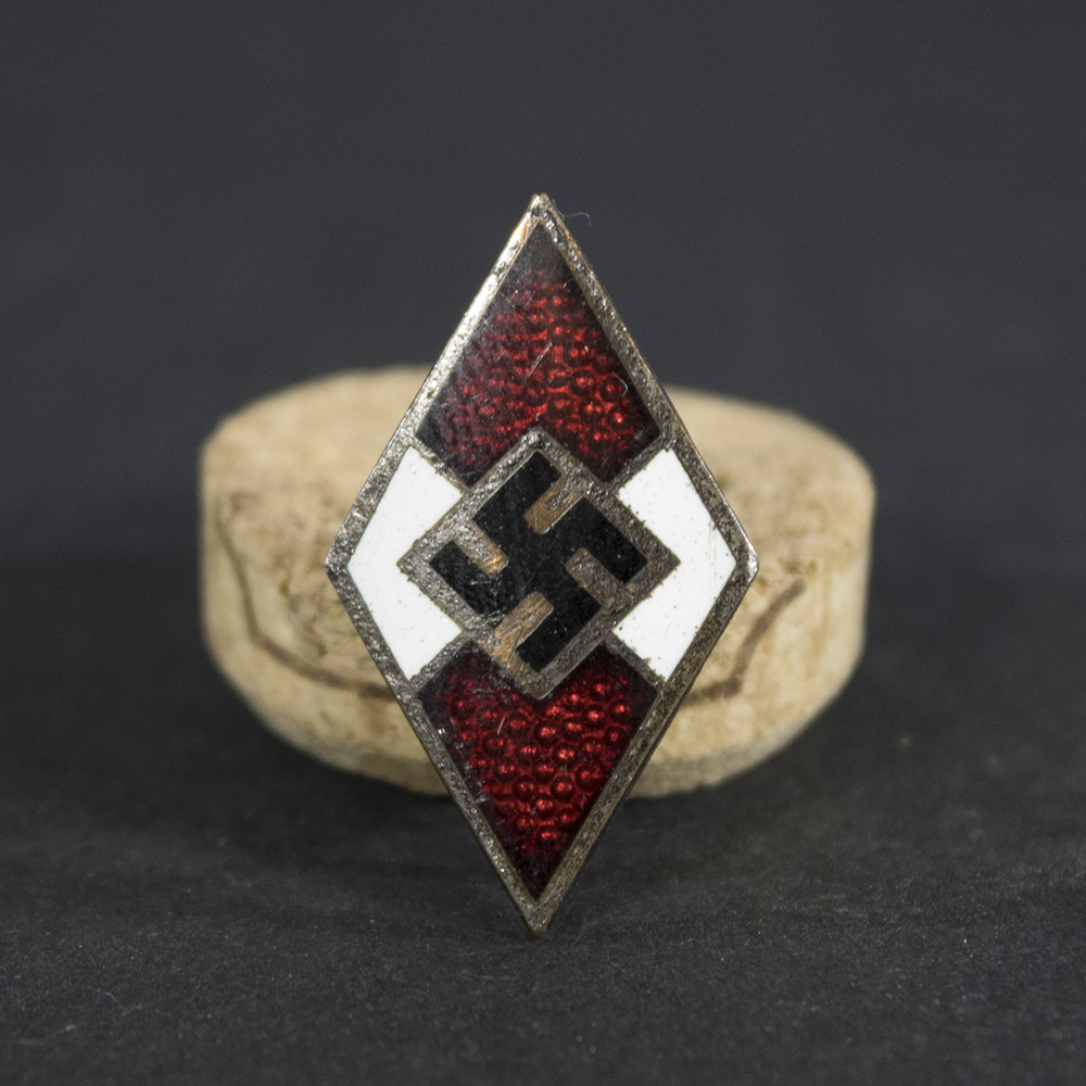 Front of a Hitler Youth membership diamond badge showing a diamond-shaped design with a white enamel border, red enamel fields at the top and bottom, and a black swastika centered on a white background.