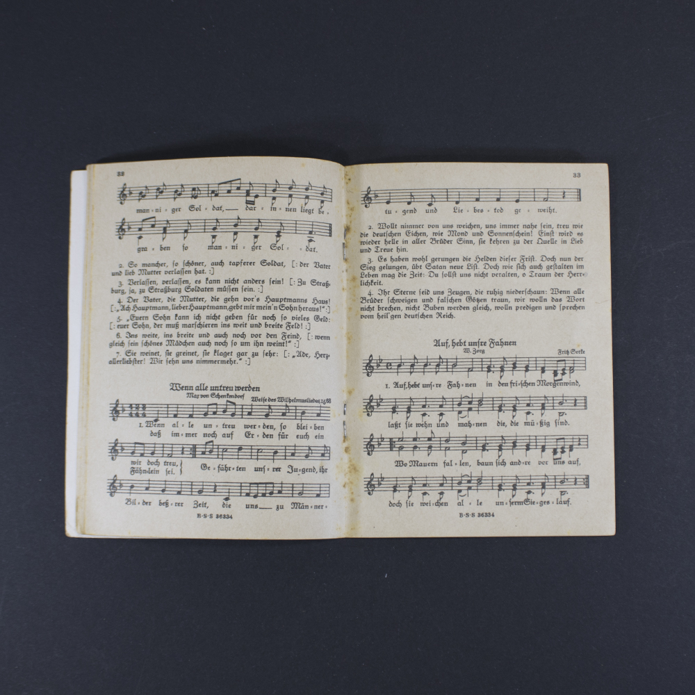 Open pages of the songbook ‘Das neue Soldaten Liederbuch’ displaying printed lyrics in Gothic typeface with musical notation above the text.