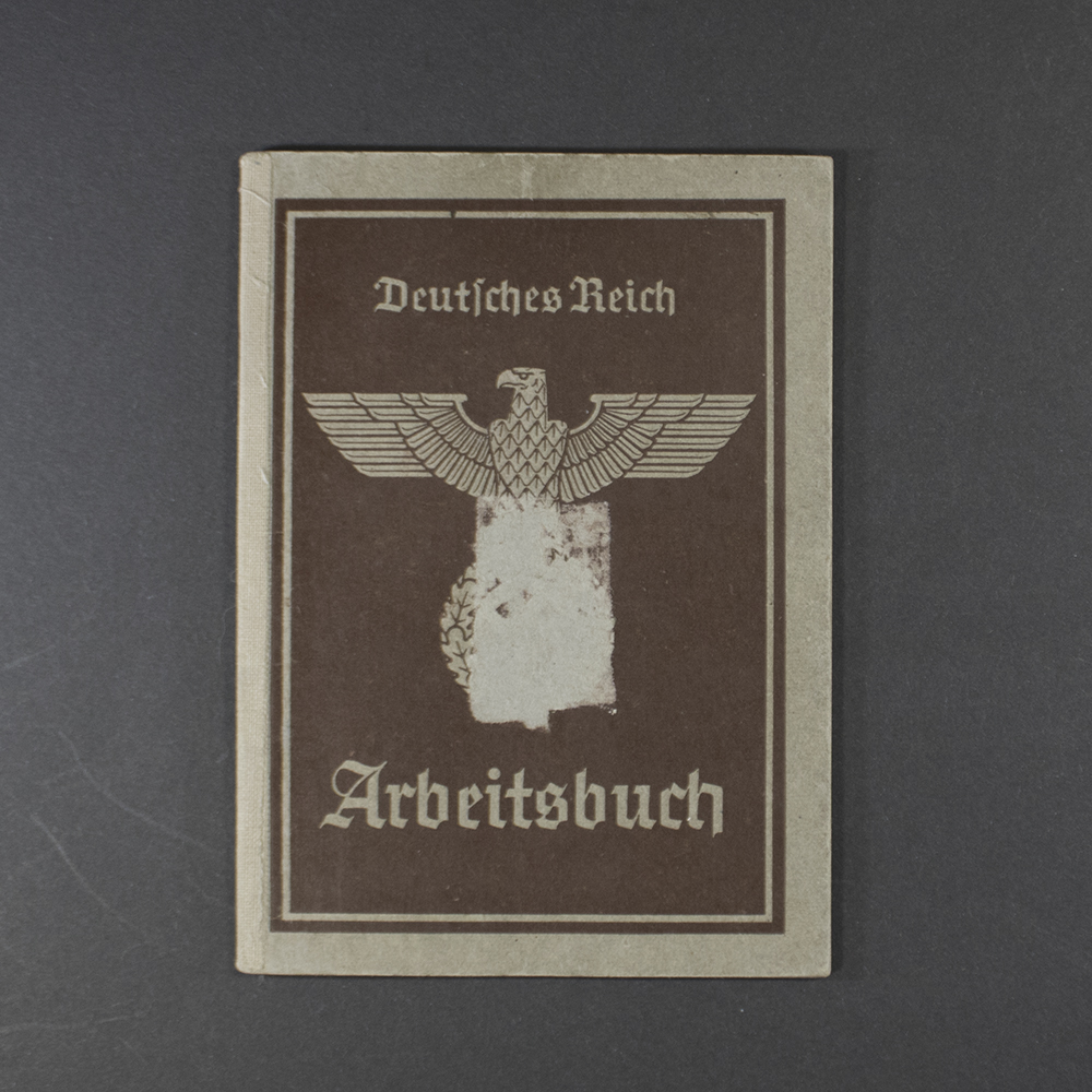 A worn, grayish-brown cover with the title “Arbeitsbuch” printed in bold black letters. Below the title is an eagle and swastika emblem, with official stamps and a serial number. The paper shows heavy creases and discoloration from age.