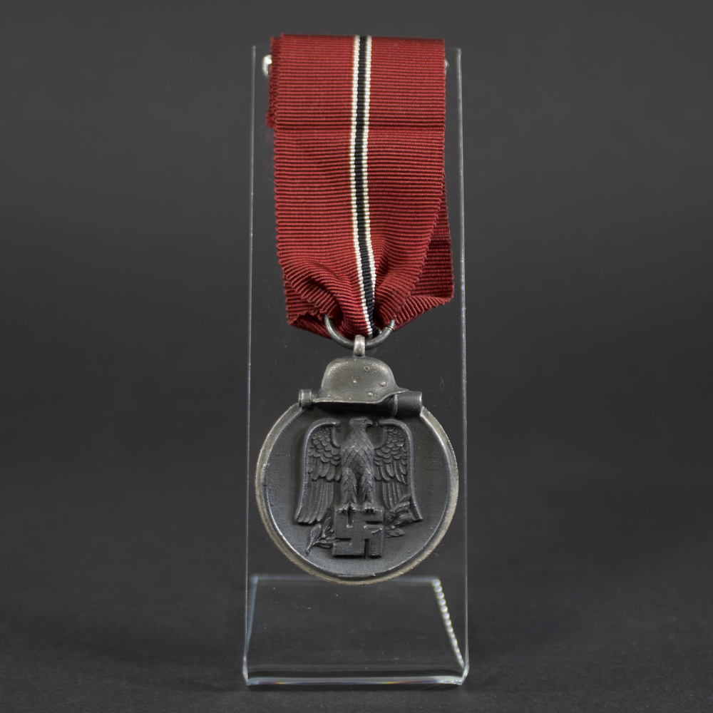 A WWII German Eastern Front Medal with a dark gray finish and a suspension ring at the top. The medal is oval-shaped and shows signs of age.