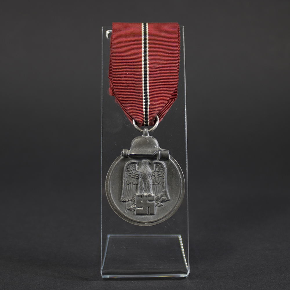 A WWII German Eastern Front Medal with a dark gray finish and a suspension ring at the top. The medal is oval-shaped and shows signs of age.