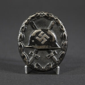 A German WWII wound badge, oval-shaped with a helmet and crossed swords in relief, dark metal finish.