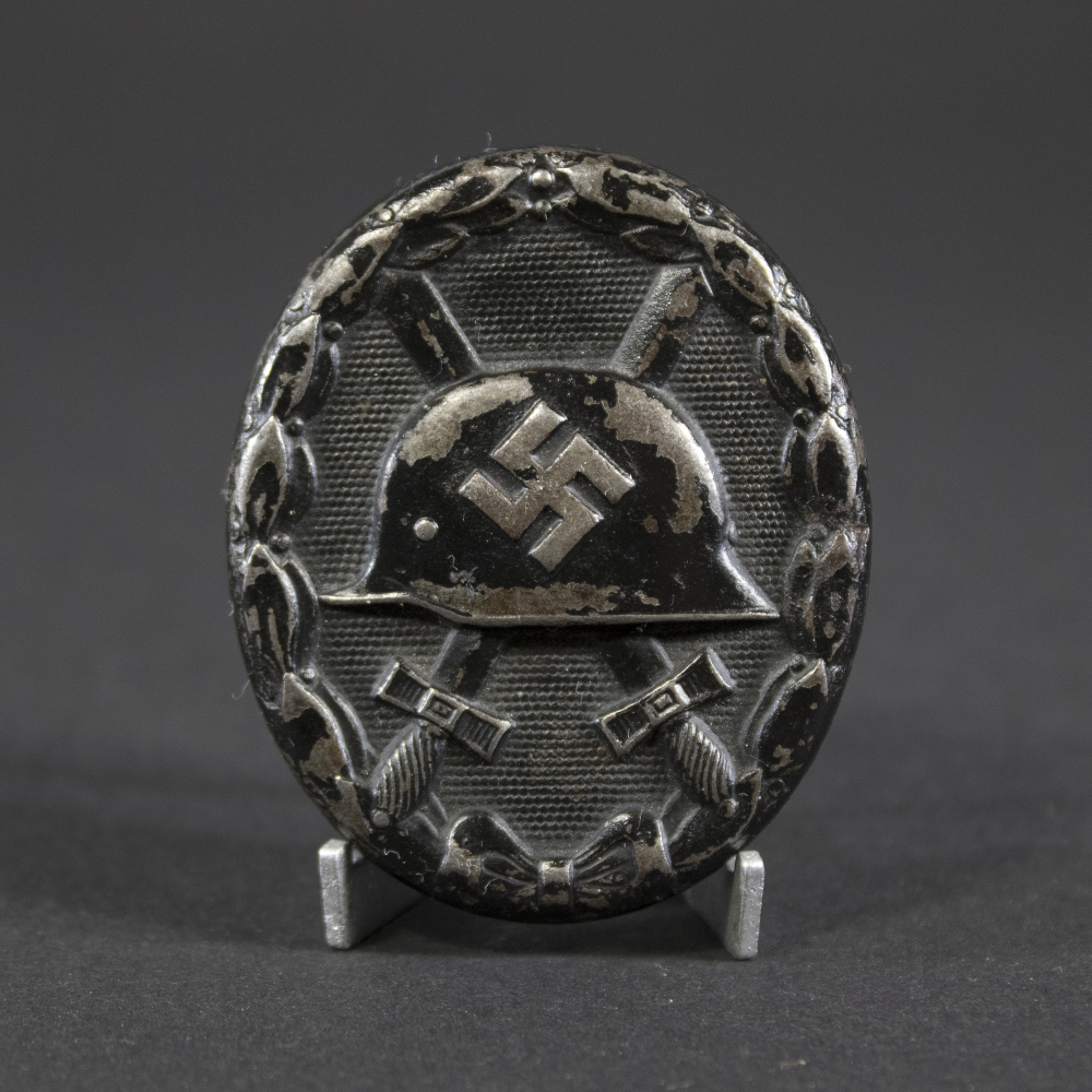 A German WWII wound badge, oval-shaped with a helmet and crossed swords in relief, dark metal finish.