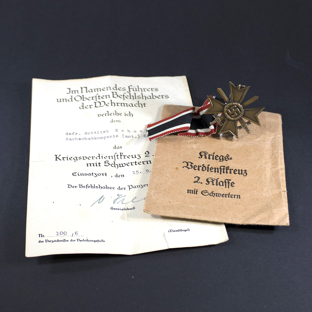 A WWII German War Merit Cross with swords displayed alongside its official award document. The bronze-toned medal hangs from a ribbon, and the document is printed in German with handwritten details.
