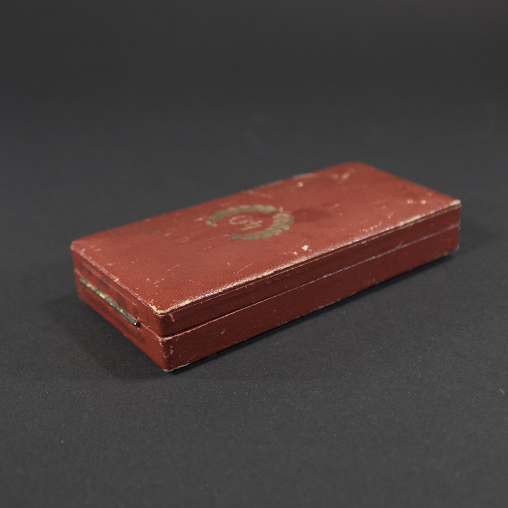 Images showing the case from different angles, highlighting its hinged structure and worn edges. The interior lining and ribbon placement are partially visible.