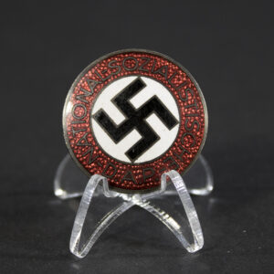 A circular NSDAP membership badge with a red enamel outer ring, white center, and black swastika. The text “Nationalsozialistische D.A.P.” encircles the center.