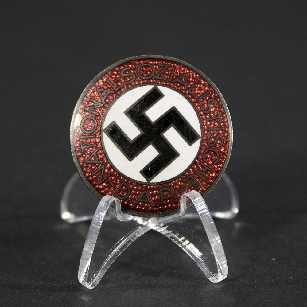 A circular NSDAP membership badge with a red enamel outer ring, white center, and black swastika. The text “Nationalsozialistische D.A.P.” encircles the center.