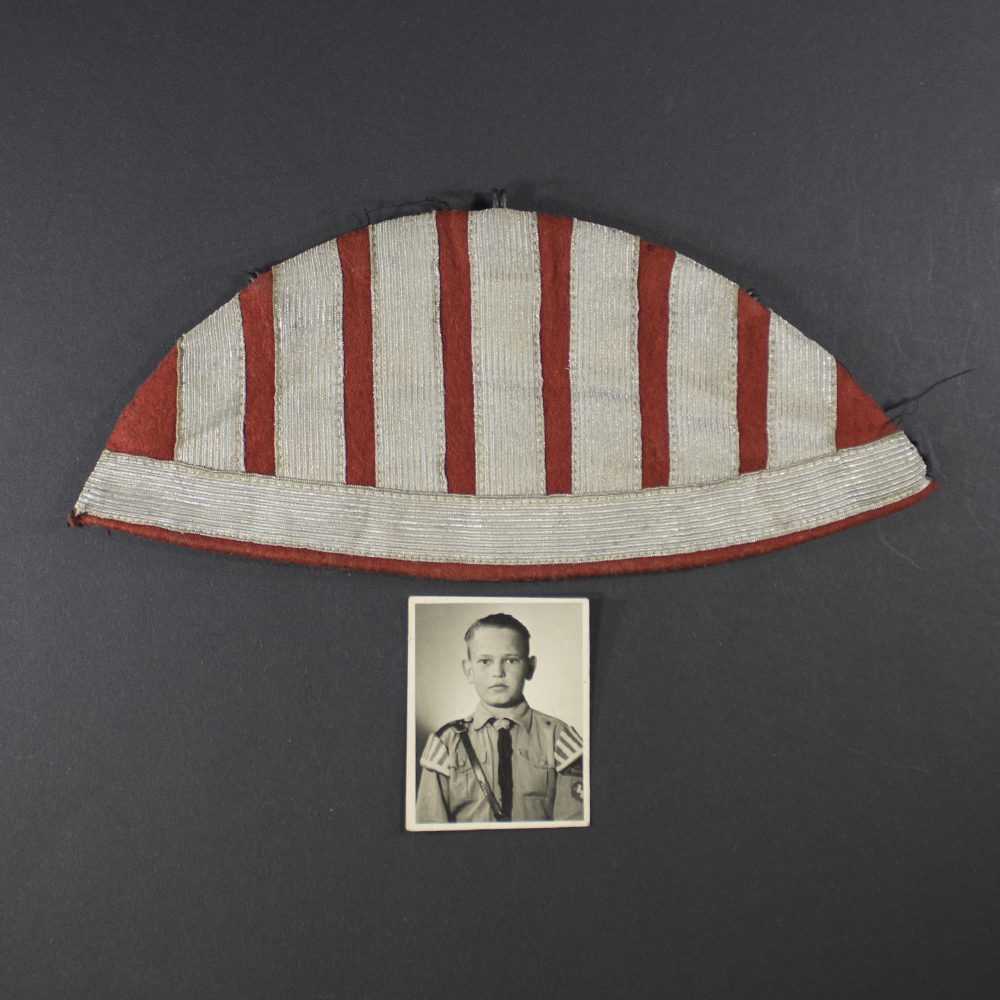 “Overview of a Hitler Youth ‘Schwalbennest’ insignia displayed alongside a portrait photograph. The insignia is a small, swallow-tail shaped cloth patch with embroidered details, placed near the photo of a young Hitler Youth member in uniform.”