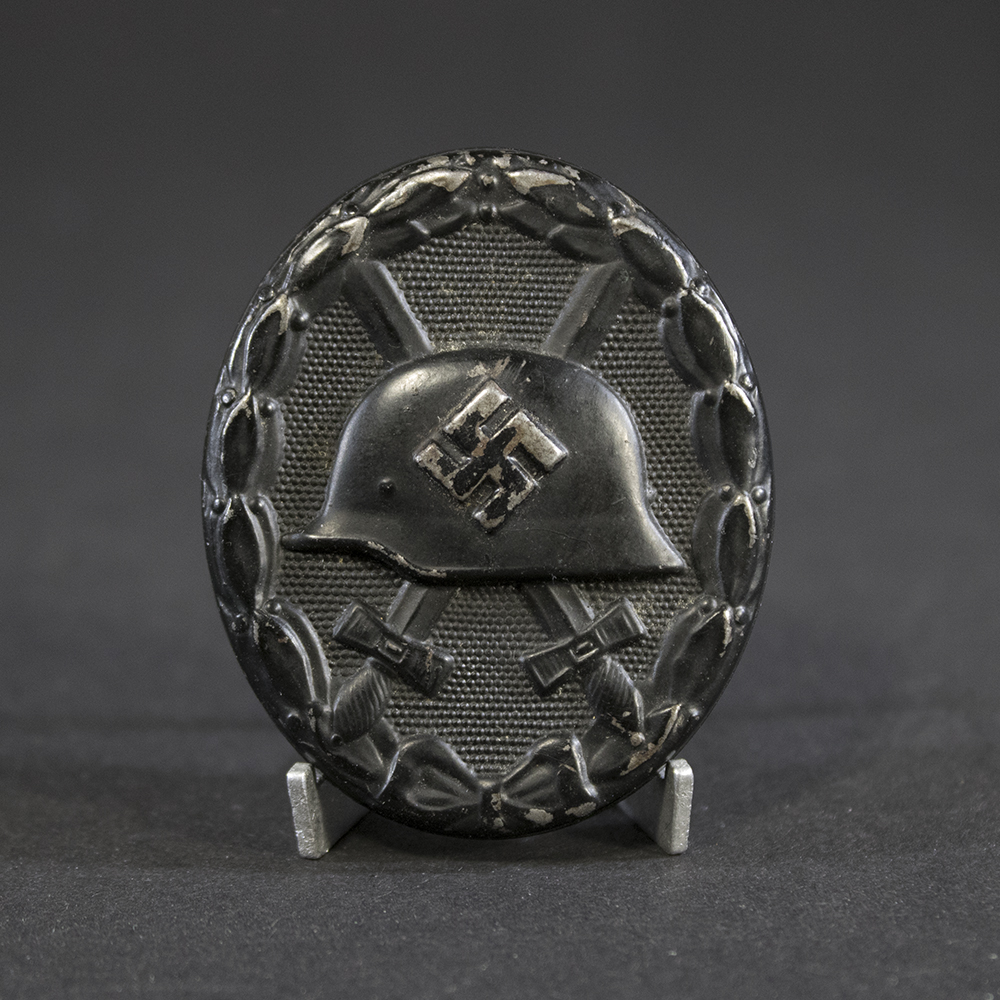 “Full view of a World War II German black wound badge, oval-shaped with a raised design featuring a helmet over crossed swords, surrounded by a laurel wreath.”
