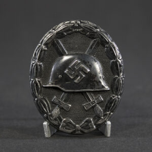 “Full view of a World War II German black wound badge, oval-shaped with a raised design featuring a helmet over crossed swords, surrounded by a laurel wreath.”