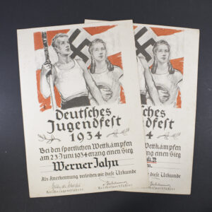 “Two award documents from the Deutsches Jugendfest 1934 displayed side by side. Each document features ornate borders, Gothic-style German text, and official emblems, printed on aged paper.”