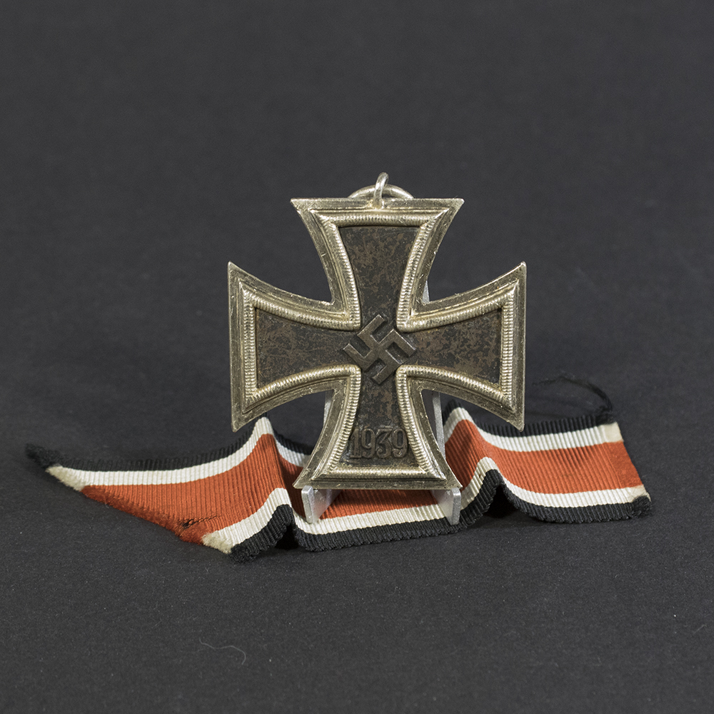 World War II German Iron Cross 2nd Class medal with attached ribbon, displayed flat. The cross features a black core with silver edges and a central swastika.