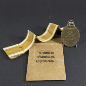 Full view of a World War II German Westwall Medal placed alongside its original paper bag, showing the bronze-colored medal and the simple brown bag
