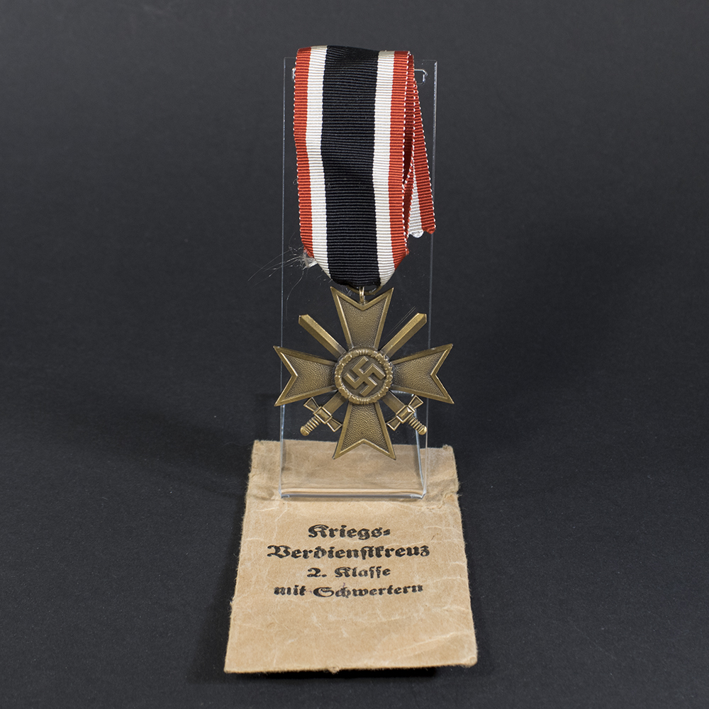 Full view of a World War II German War Merit Cross with swords displayed alongside its original brown paper bag.