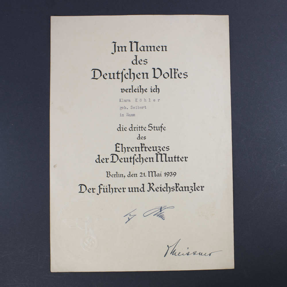 Front view of a World War II German award document for the Bronze Mother’s Cross, featuring printed German text in Gothic script, official stamp, and handwritten signature.