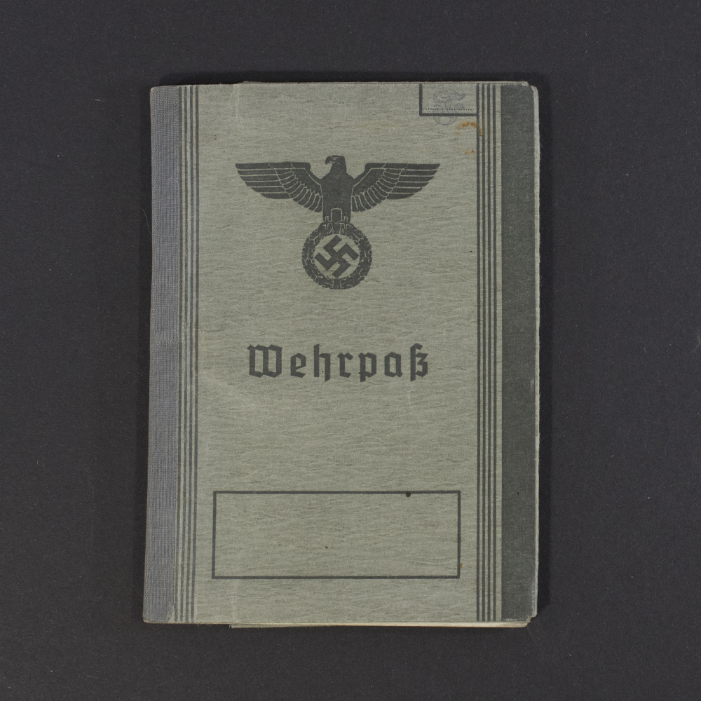 Front cover of a World War II German Wehrpass, showing the gray textured surface with the eagle and swastika emblem above the word ‘Wehrpass.