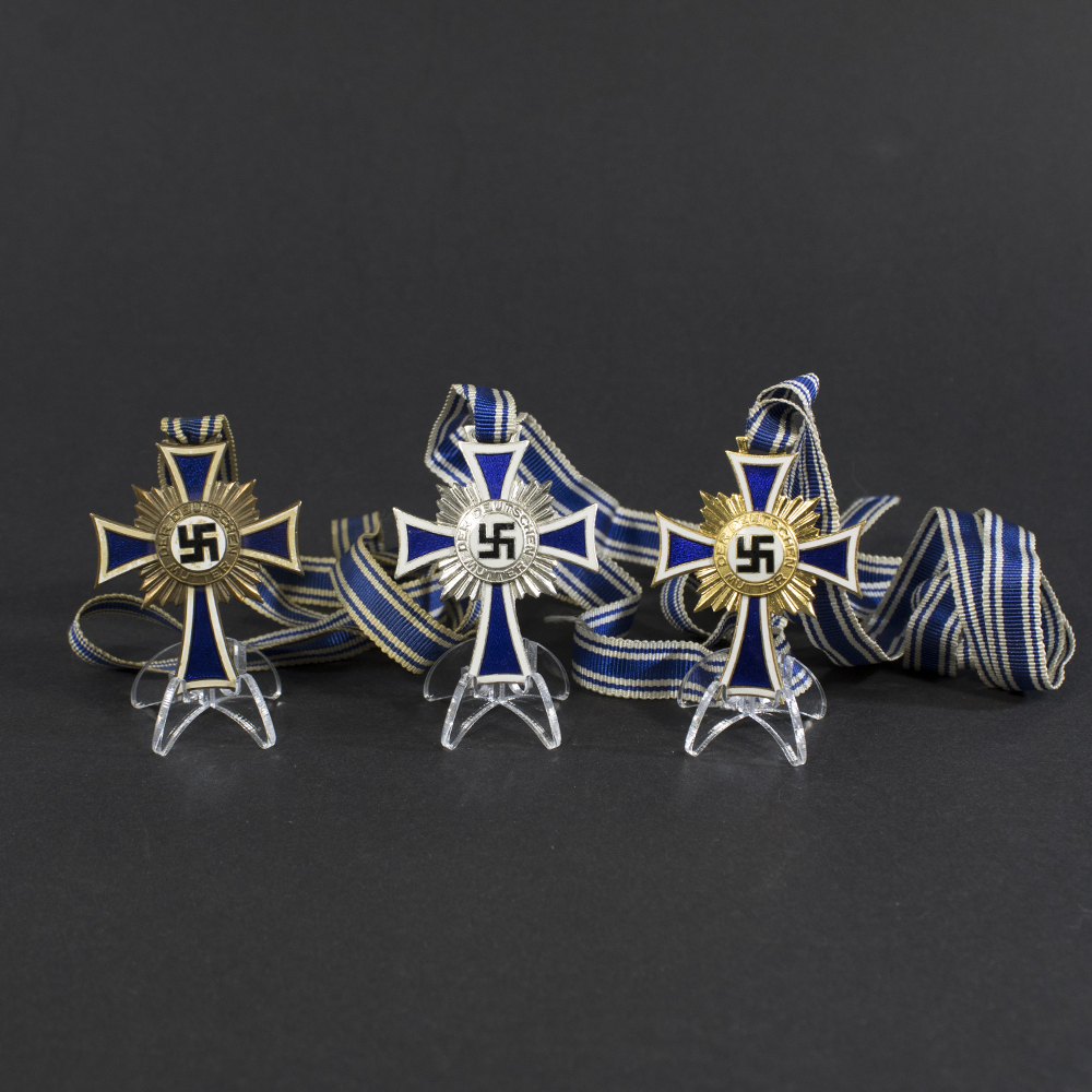 A complete set of World War II German Mother’s Cross awards in bronze, silver, and gold grades, each featuring a blue and white enamel cross with a central swastika and ribbon.