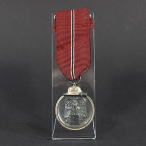 A World War II German Eastern Front Medal displayed in full view, showing its oval shape with a loop at the top for suspension. The medal features a darkened finish and a ribbon attached.