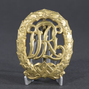 Front view of a World War II German golden DRL sports badge, featuring an ornate monogram of the letters ‘DRL’ surrounded by a laurel wreath with a gold finish.