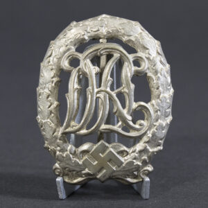 Front view of a World War II German silver DRL sports badge, featuring an ornate monogram of the letters ‘DRL’ surrounded by a laurel wreath with a silver finish.