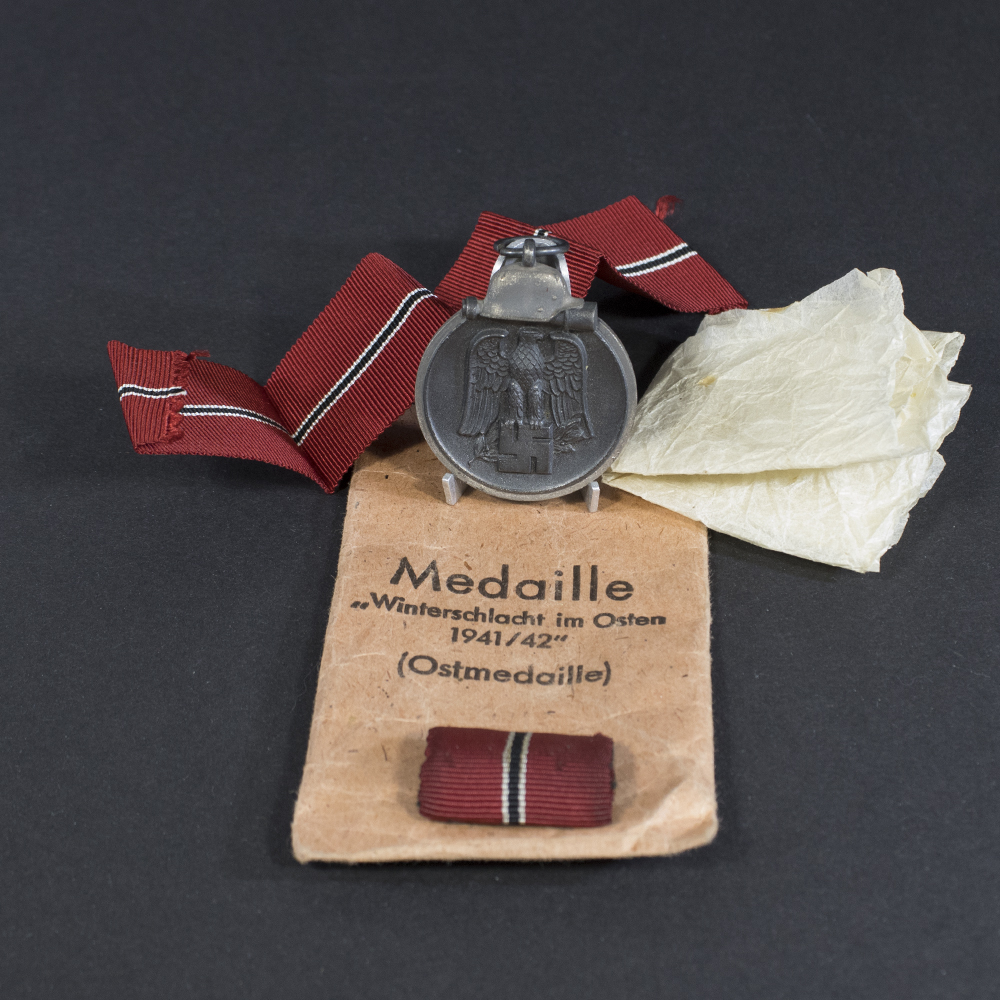 Full view of a World War II German Eastern Front Medal displayed alongside its original brown paper bag