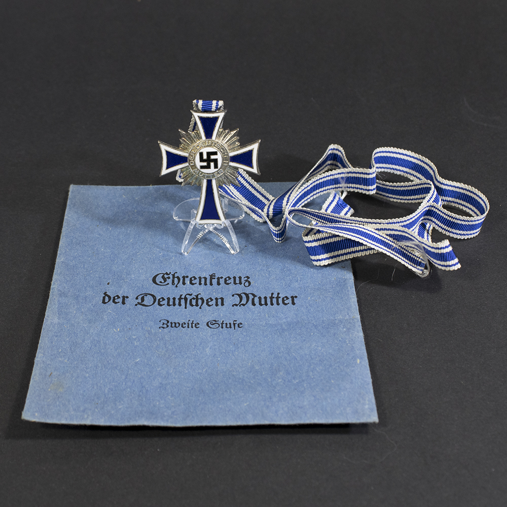 Full view of a World War II German Silver Mother’s Cross displayed alongside its original blue paper bag.