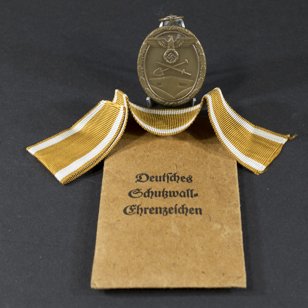 Complete World War II German Westwall medal set displayed on a flat surface, including the medal and its original paper bag.