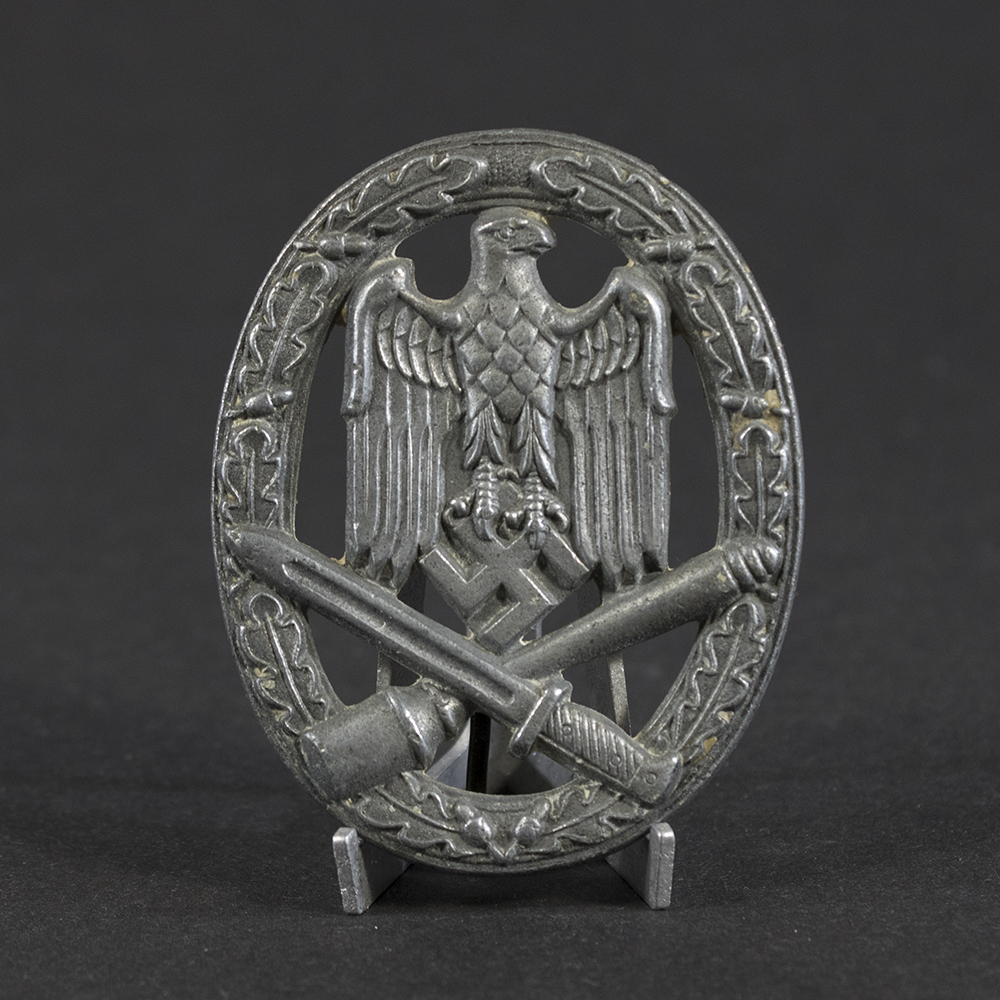 Overview of a WWII German General Assault Badge, oval-shaped metal badge featuring an eagle and crossed weapons surrounded by a wreath.