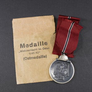 World War II German Eastern Front Medal with its original paper bag displayed together on a flat surface.