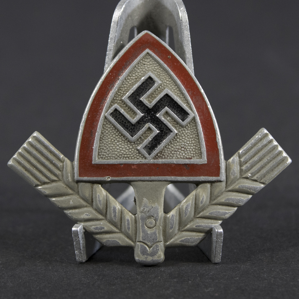 Close-up of the front of a WWII German RAD cap badge, showing the detailed spade-and-wheat motif.