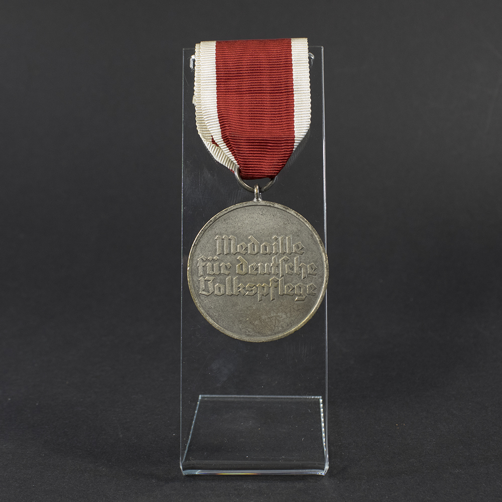 Back side of the WWII German Volkspflege Medal displayed flat, showing smooth surface with embossed inscription and aged patina.