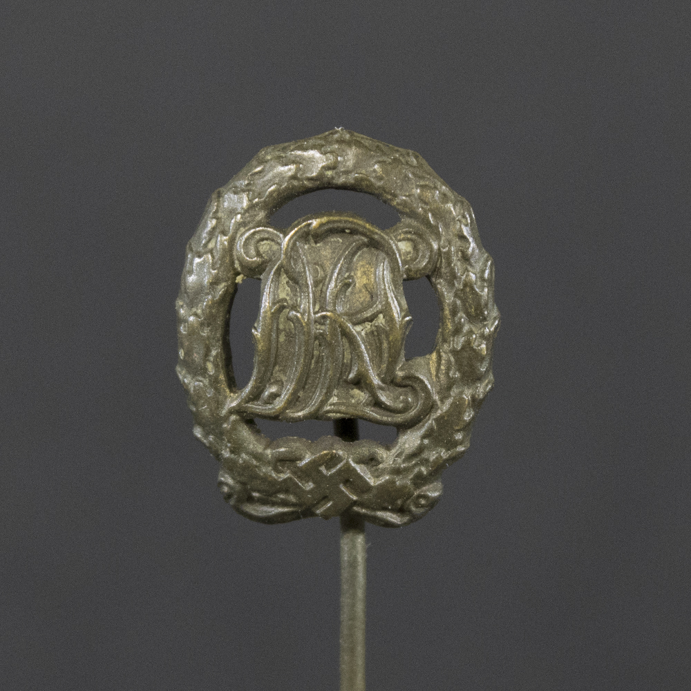 Front side of the WWII German Bronze DRL stick pin, featuring the detailed monogram design with bronze finish and visible texture.
