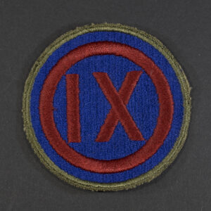 Front of WWII U.S. Army 9th Corps patch with green backing, showing shield shape and insignia in good condition.