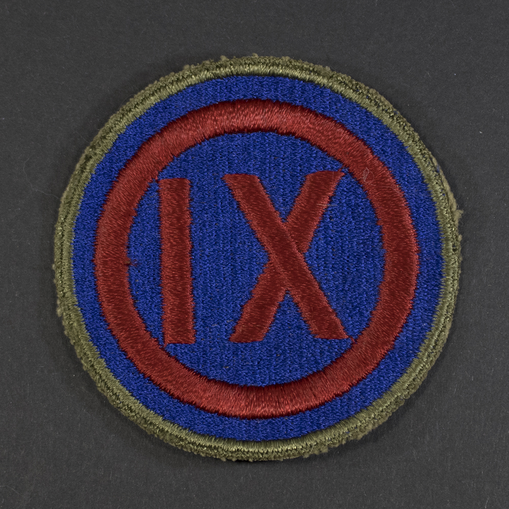 Front of WWII U.S. Army 9th Corps patch with green backing, showing shield shape and insignia in good condition.