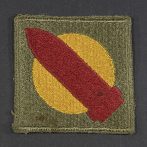 Front of WWII U.S. Army 1st Coast Artillery New England patch with green backing, featuring red circle with white center and blue cannon emblem.