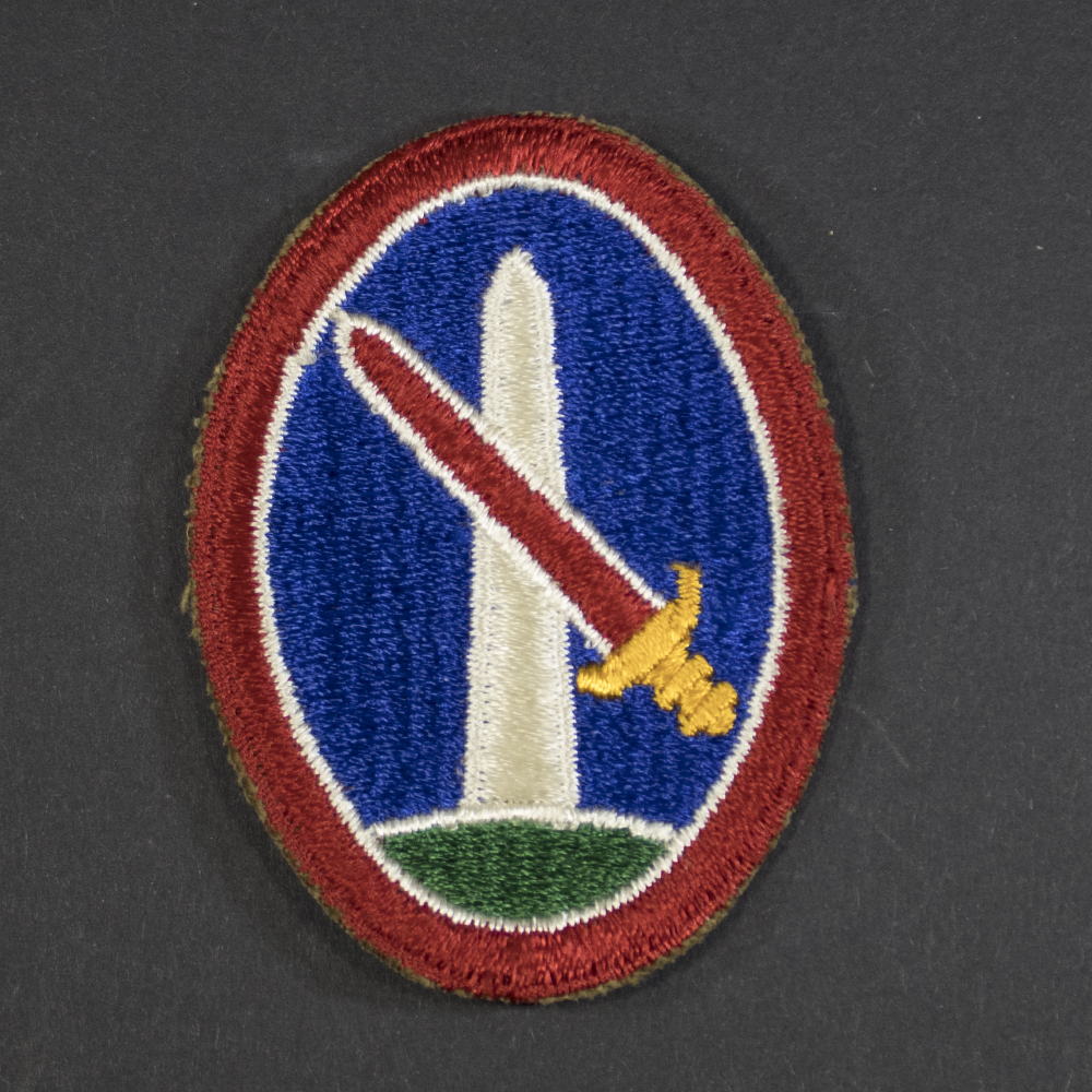 Front of WWII U.S. Army Military District of Washington patch, featuring blue shield with white star and red center, topped by U.S. Capitol dome.