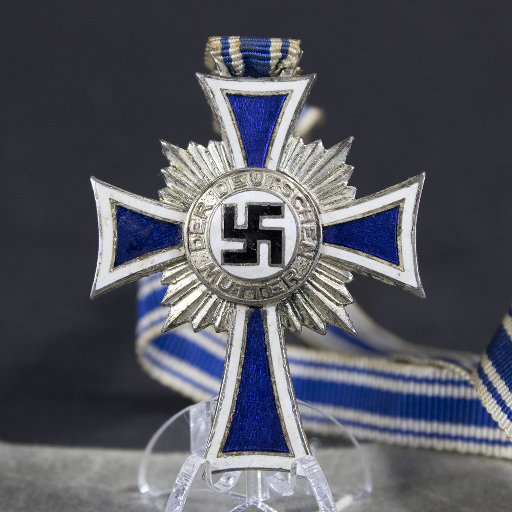 Detailed close-up of the front of the WW2 German Silver Mother’s Cross, showing the white and blue enamel rays, central black swastika in a white medallion, and the attached blue-and-white neck ribbon.