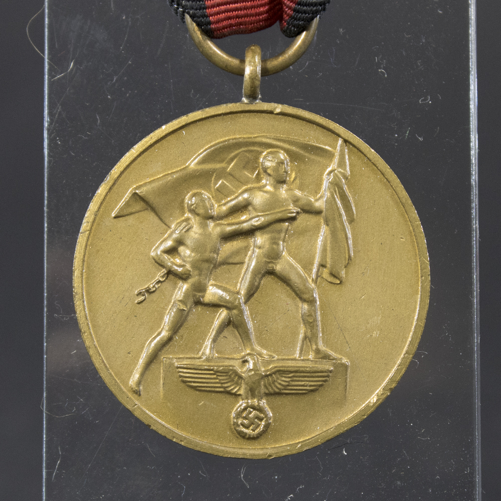 Close-up of the front of the WW2 German Sudetenland Occupation Medal, featuring the relief of two figures—one holding the Nazi flag—stepping onto a raised platform representing the annexation.