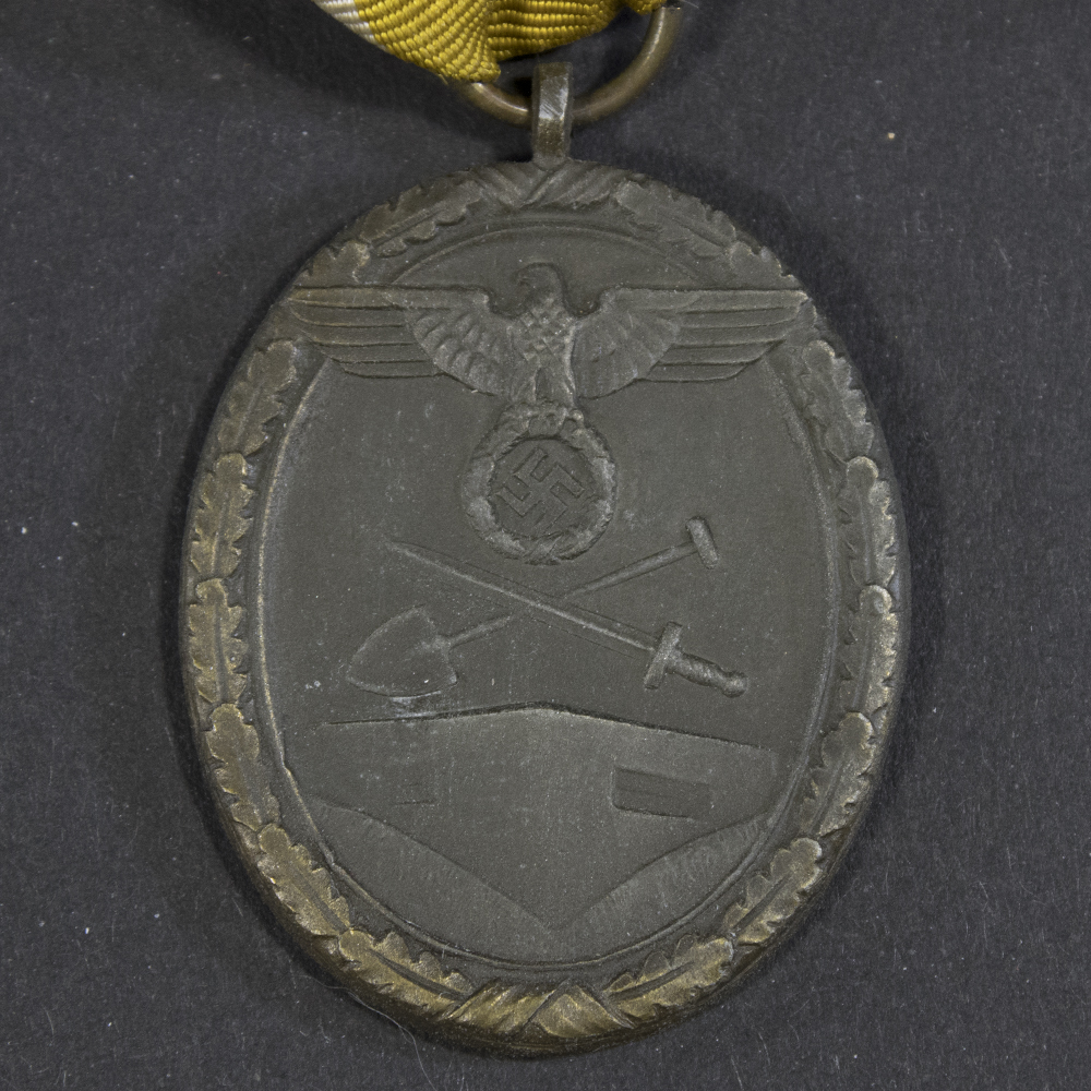 Close-up of the front of the WW2 German Westwall Medal, displaying the raised eagle and swastika above the defensive wall motif.