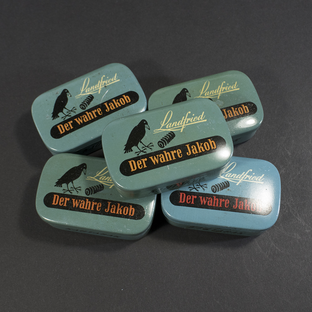 Group photo showing five original WW2 Landfried ‘Kautabak’ metal tobacco cans, displayed together to highlight the slight color variations between them.