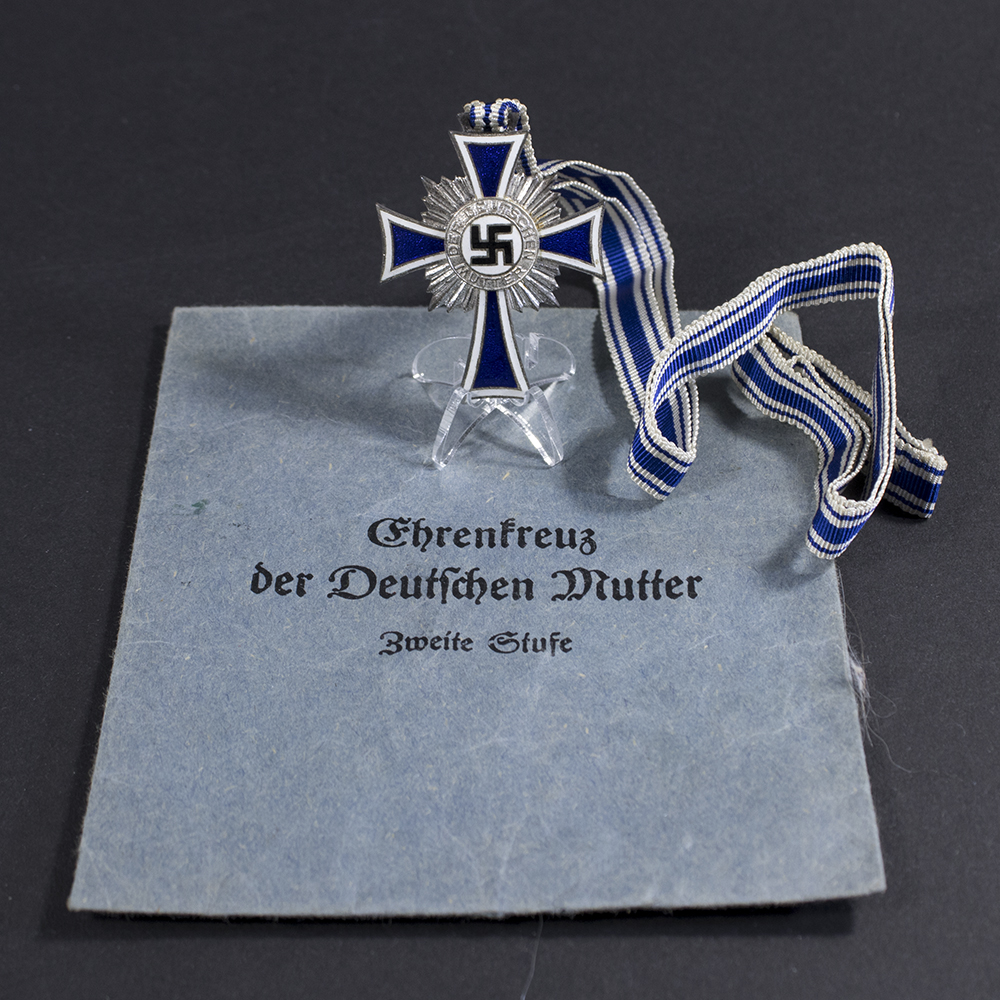 Overview of a WWII German silver Mother’s Cross set, showing the medal with its ribbon alongside the original cloth bag.