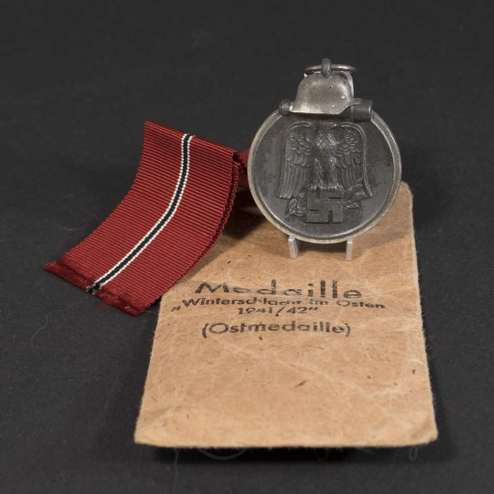 Overview of a WWII German Eastern Front Medal displayed together with its original paper issue bag