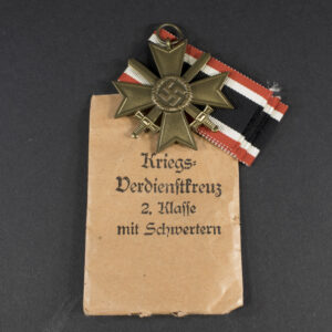 German WWII War Merit Cross with Swords set displayed with original paper bag, showing medal, ribbon, and packaging together.