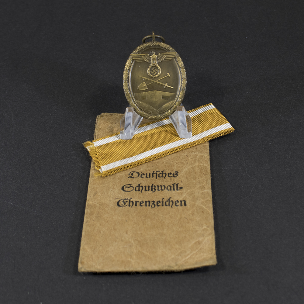 Overview of a WWII German West Wall Medal displayed together with its original issue bag.